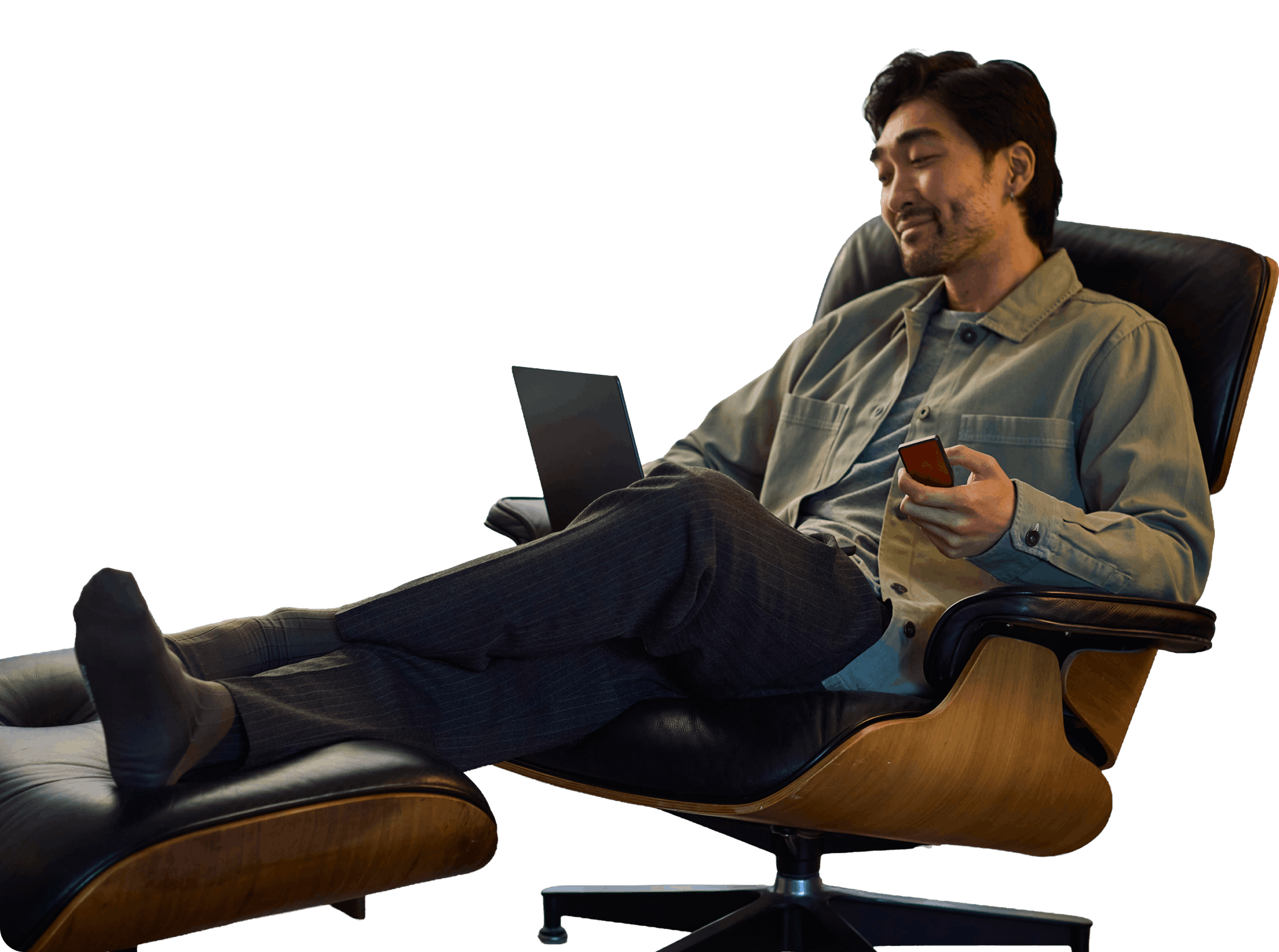 Relaxed man reclining in a wooden lounge chair, using a laptop and holding a smartphone against a black background.